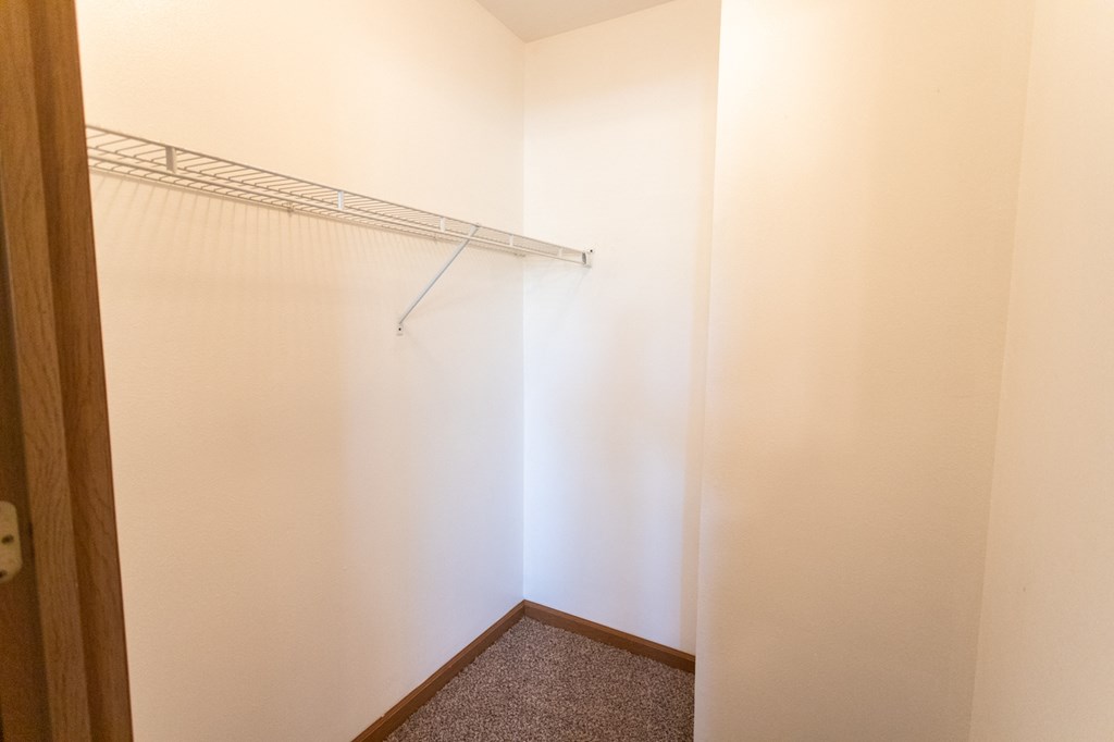 a walk in closet with a white wall and a hanging rack