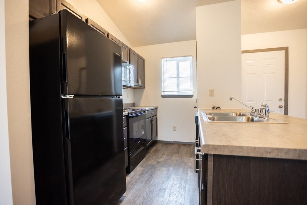 an empty kitchen with a black refrigerator and a sink