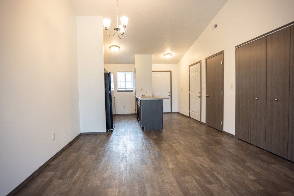 an empty living room and kitchen with wood floors and white walls
