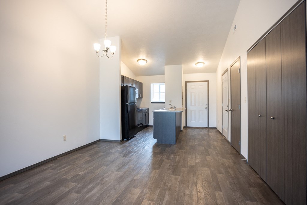 an empty living room and kitchen with wood flooring and white walls
