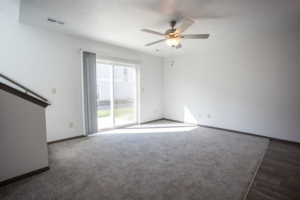 an empty living room with a ceiling fan and a window