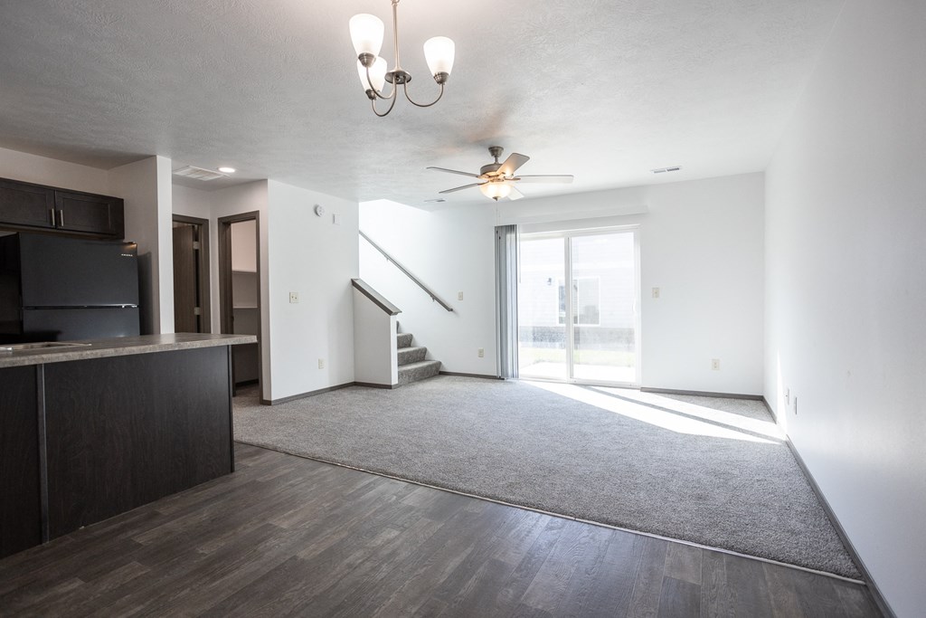 an empty living room with a kitchen and a ceiling fan