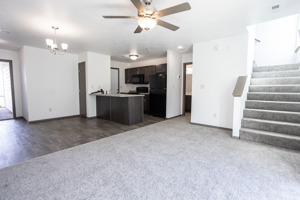 an empty living room and kitchen with stairs and a ceiling fan