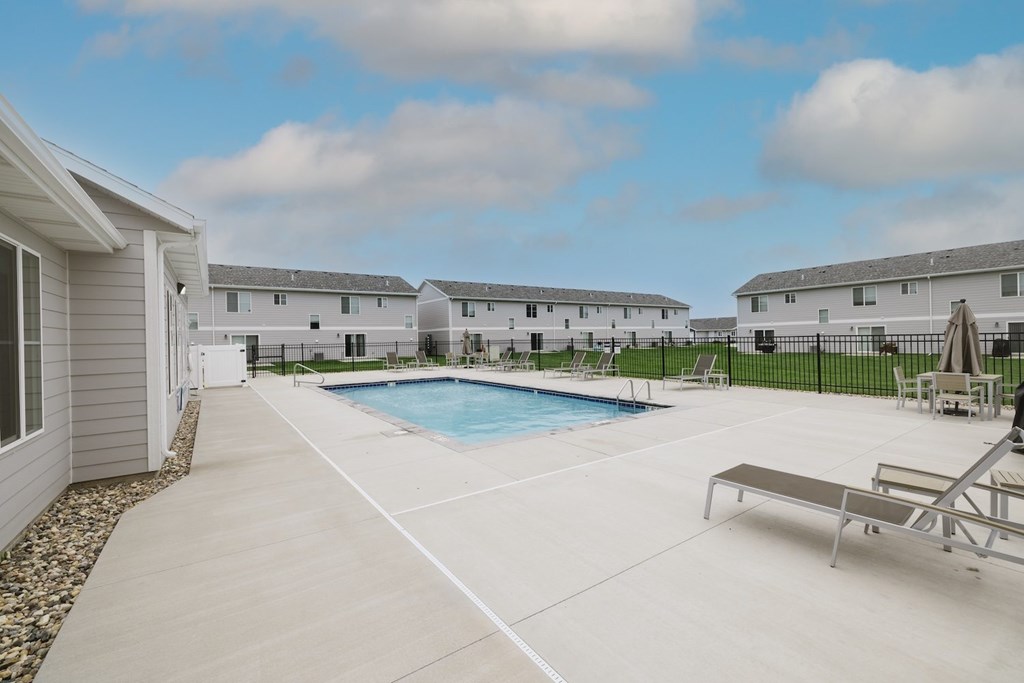 A swimming pool in a residential area with a bench and a fence.