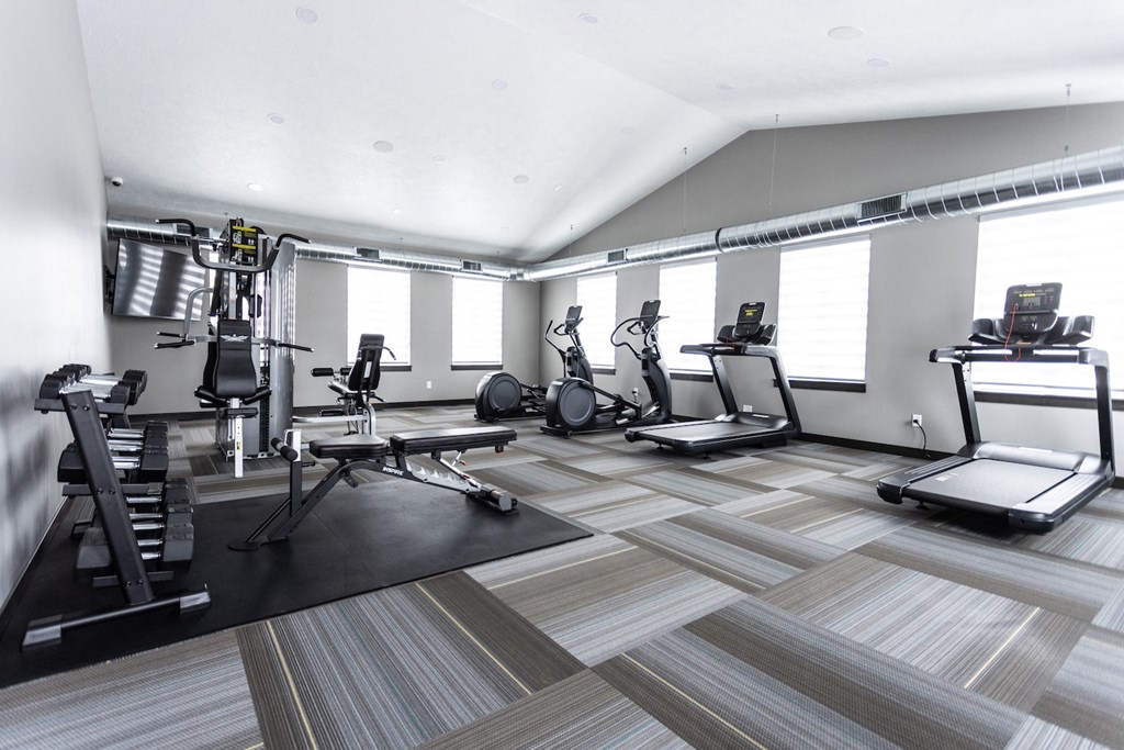 a gym with treadmills and other exercise equipment in a room with windows
