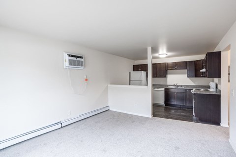 an empty living room with a kitchen in the background