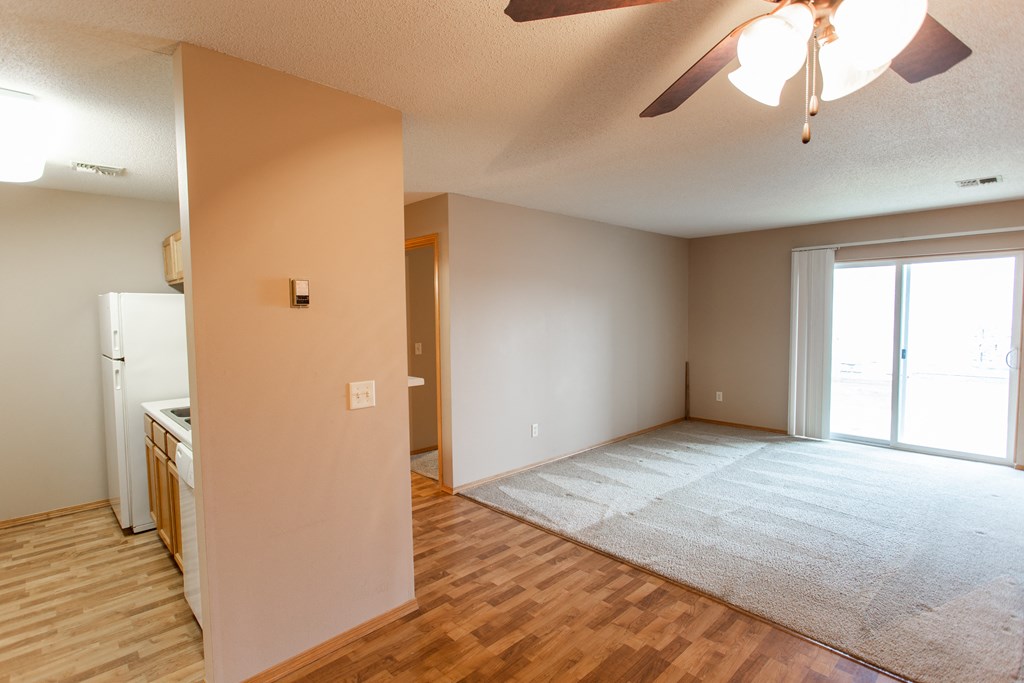 an empty living room with a kitchen and a ceiling fan