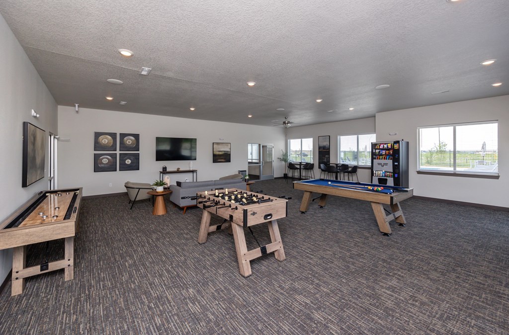 A room with a pool table, air hockey table, foosball table, and a shuffleboard table.