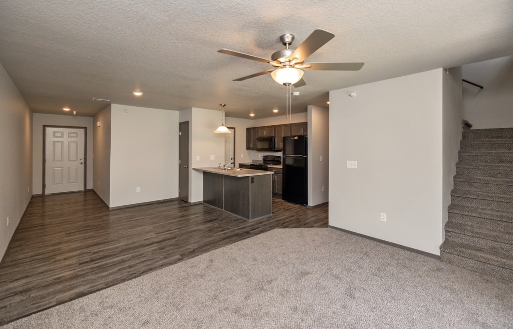 A spacious living room with a ceiling fan and a staircase.
