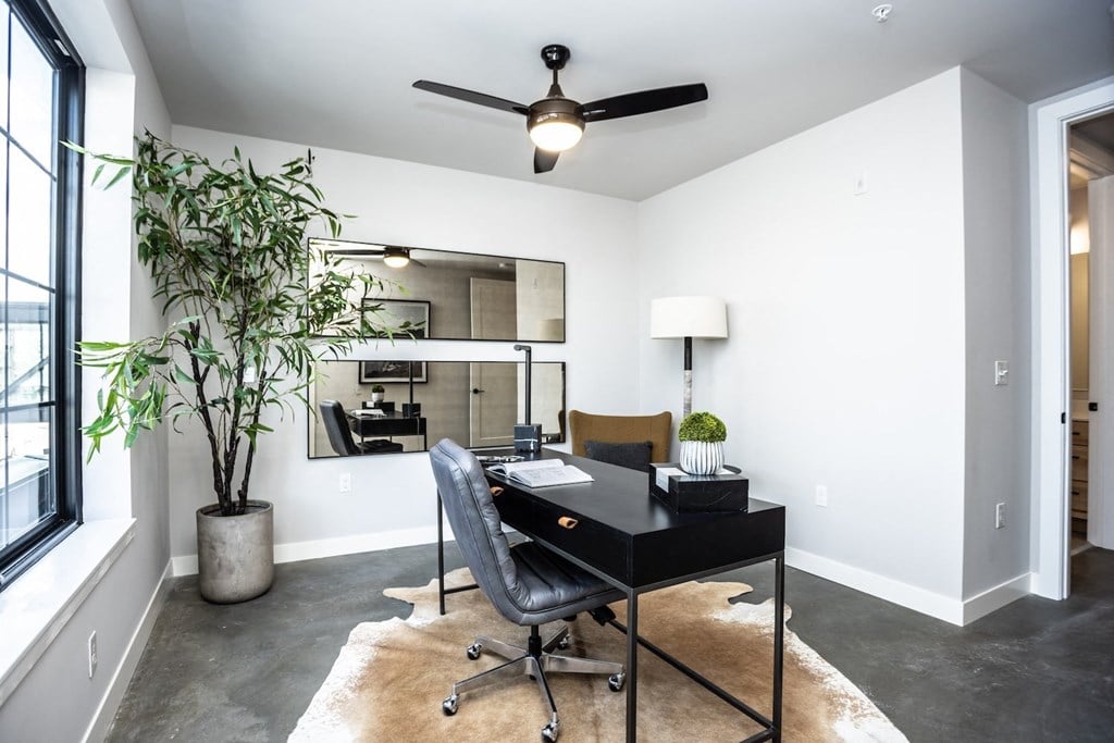 a home office with a black desk and a large window