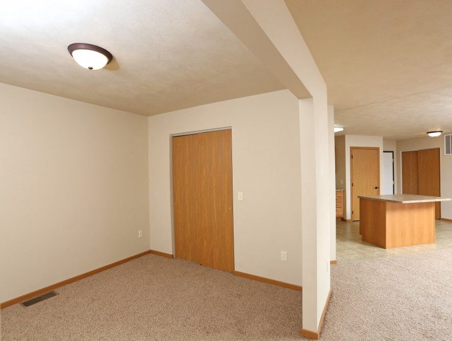 an empty living room with a door to a kitchen