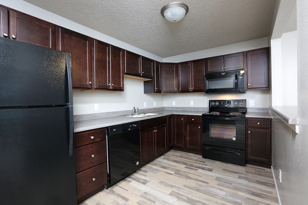 an empty kitchen with dark wood cabinets and black appliances