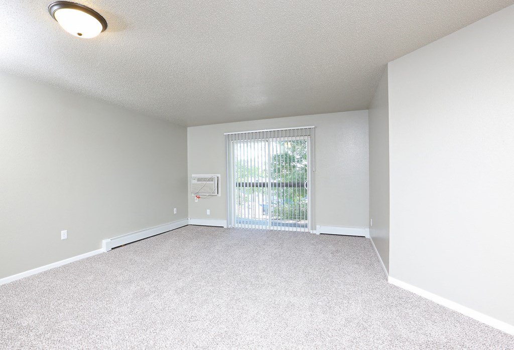 an empty living room with a large window and white carpet