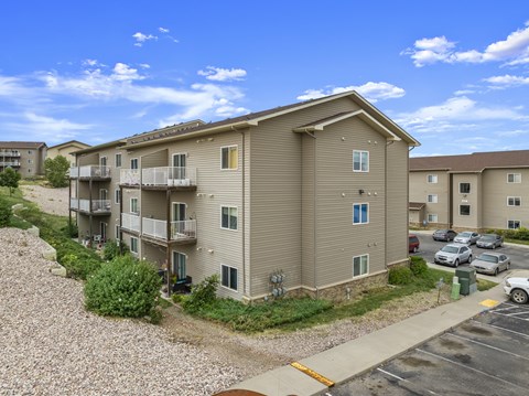 A sunny day at the apartment complex with cars parked in the parking lot.