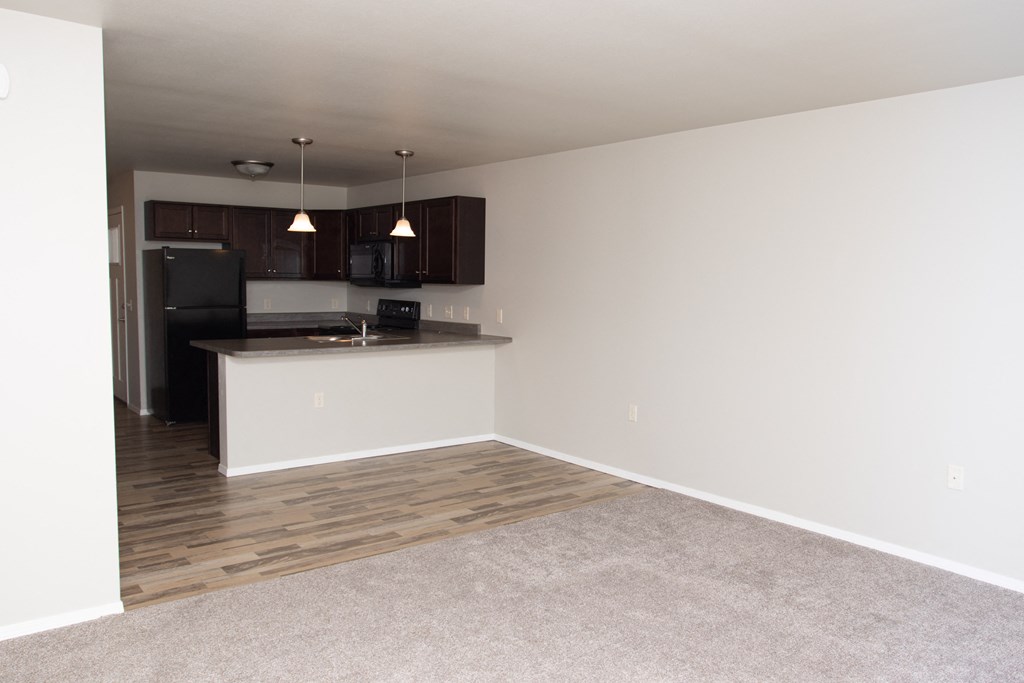 an empty living room with a kitchen and a hard wood floor