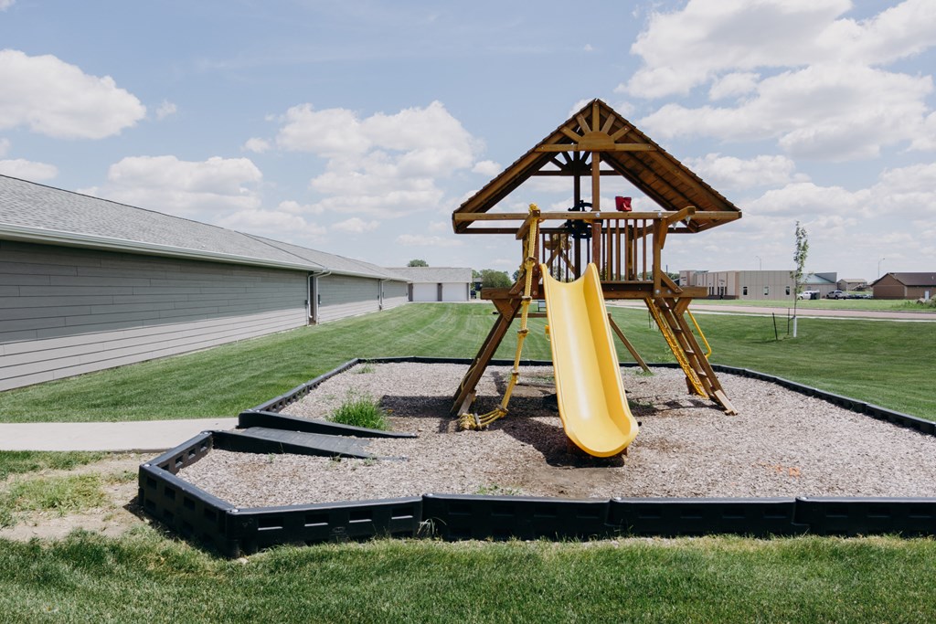 a playground with a swing set in front of a house