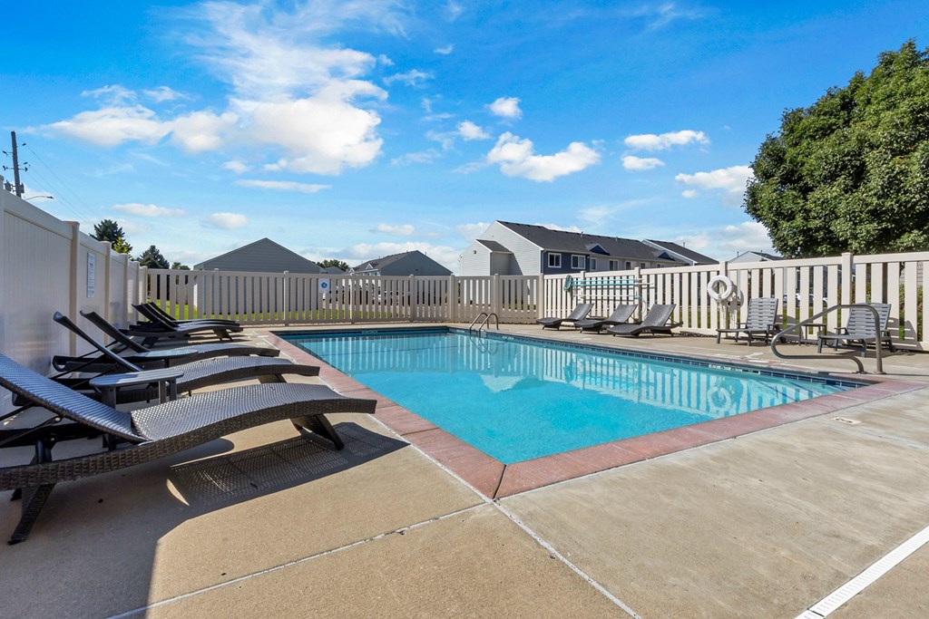 A pool with sun loungers and a fence in the background.