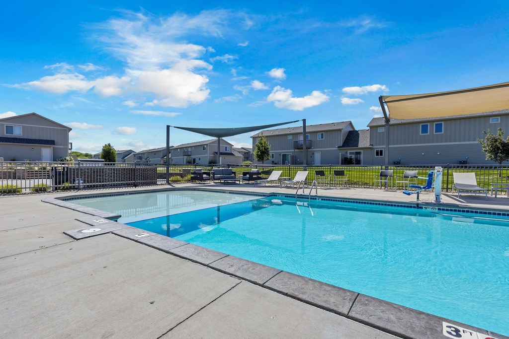 A large outdoor swimming pool with a blue sky and clouds in the background.