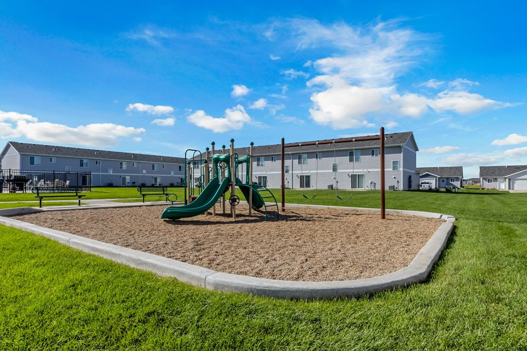 A playground with a green slide and a sandbox in the foreground.