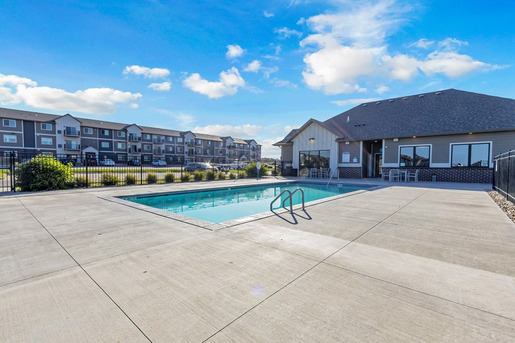 A swimming pool in a concrete pool area with a building in the background.