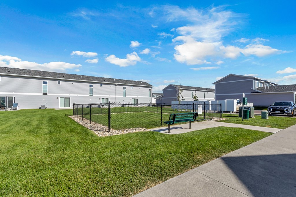 A sunny day at a park with a bench and a fence.