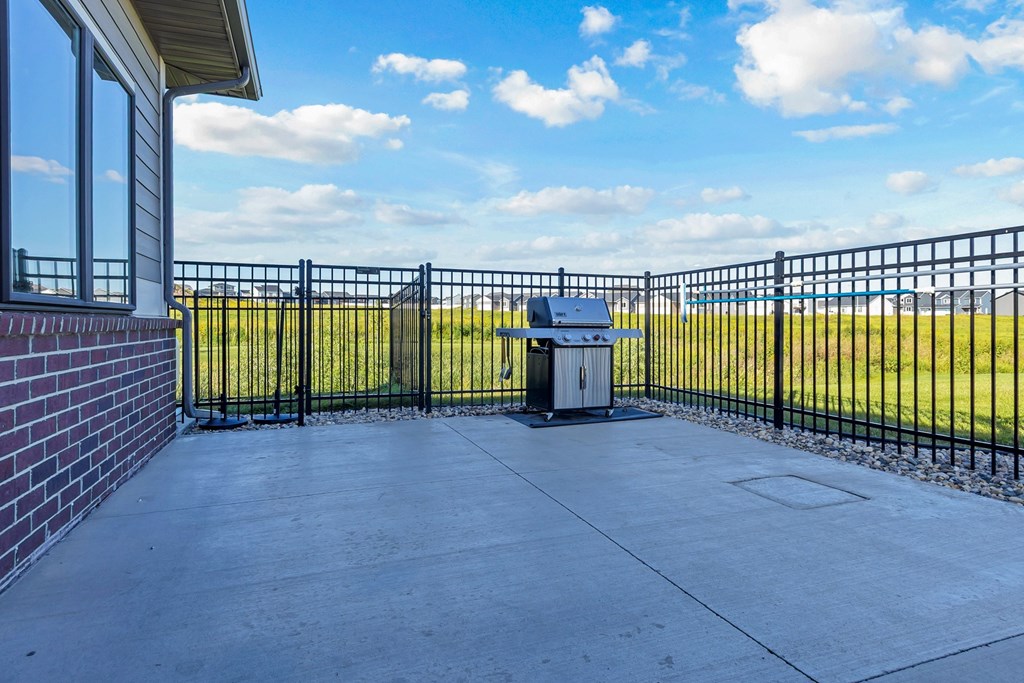 A black metal fence surrounds a concrete patio with a trash can in the middle.