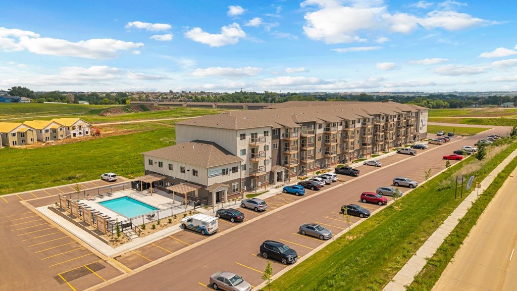 A large apartment complex with a pool and cars parked in the parking lot.