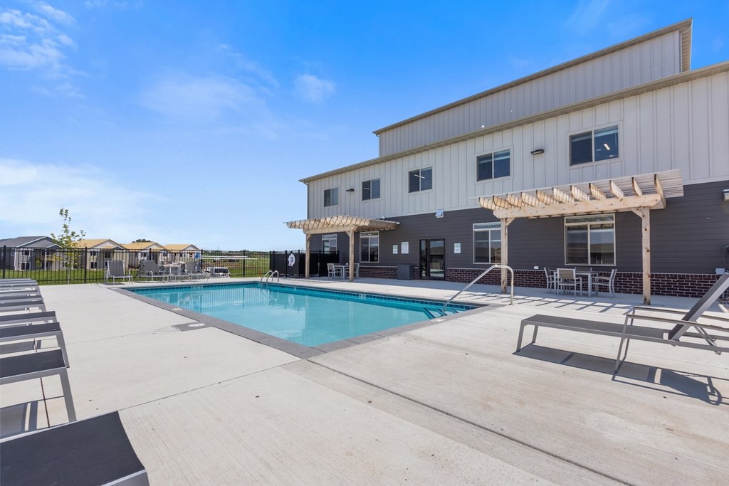 A pool area with sun loungers and a building in the background.