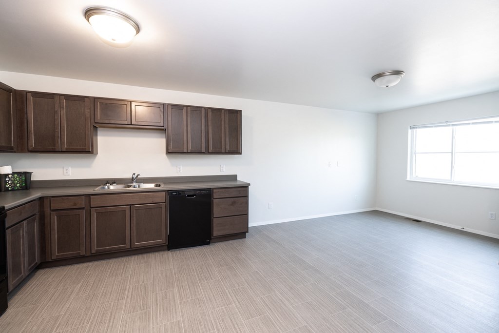 an empty kitchen and living room with wood flooring and wooden cabinets