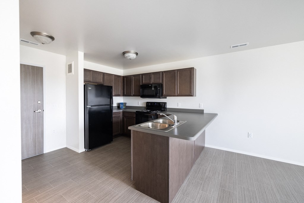 an empty apartment with a kitchen and a black refrigerator