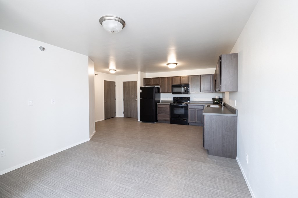 an empty living room and kitchen with black appliances and white walls