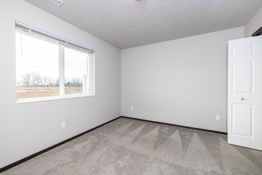A room with a carpeted floor, a window, and a white door.