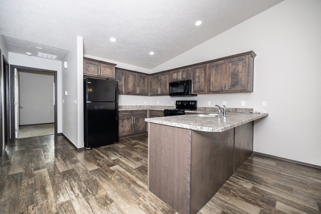 A kitchen with a black fridge and microwave, a white counter top, and wooden cabinets.