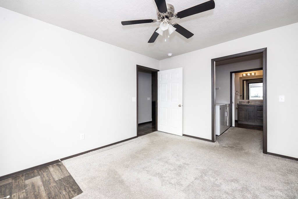 A spacious room with a ceiling fan and a door leading to a kitchen.