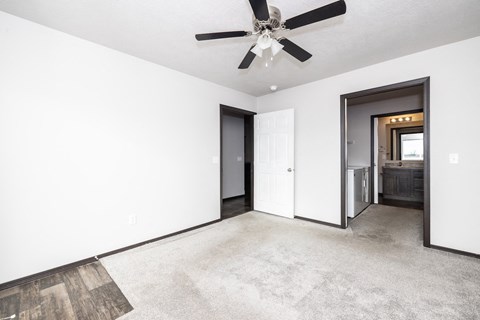 A spacious room with a ceiling fan and a door leading to a kitchen.