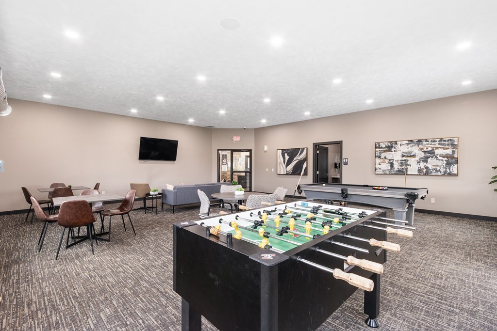 A foosball table is in the middle of a room with chairs and a TV.