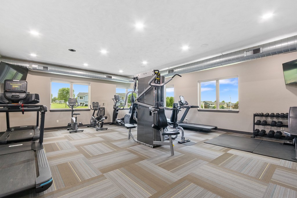 A spacious gym with a variety of equipment and a view of the outdoors through the windows.