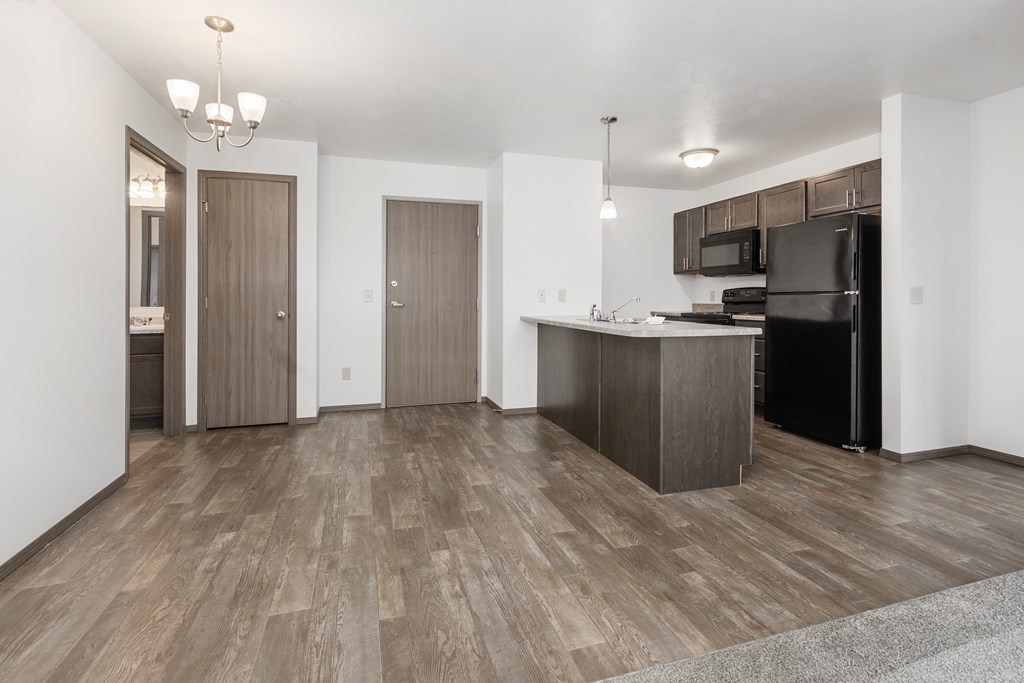 A kitchen with a black refrigerator and wooden floors.