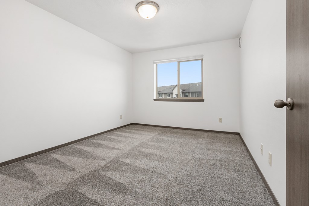 A room with a carpeted floor and a window overlooking a building.