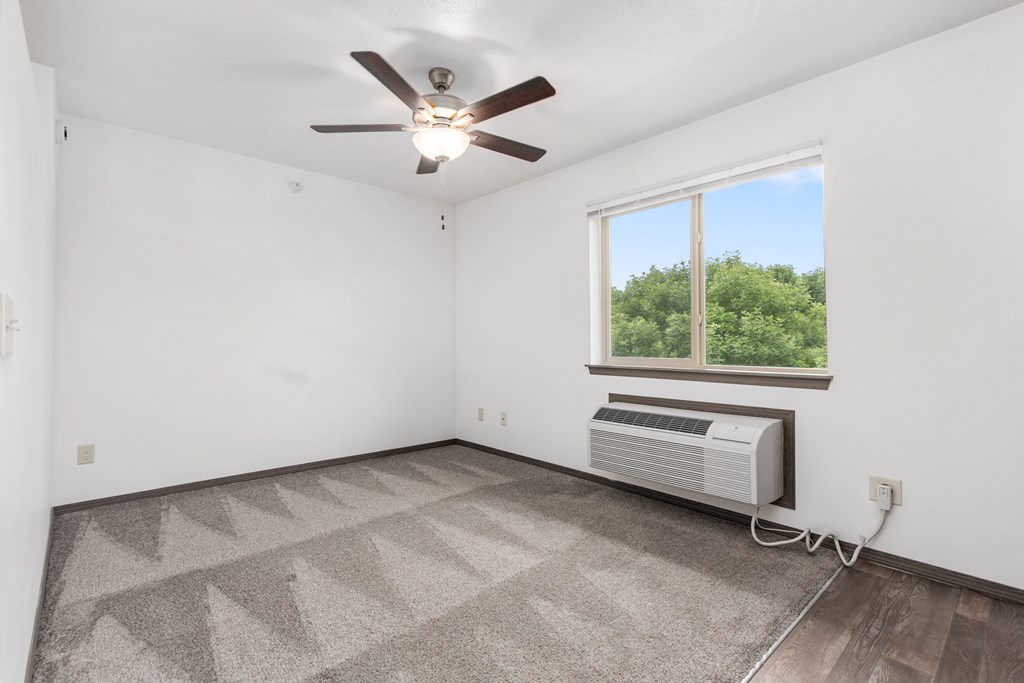 A room with a ceiling fan and a window with an air conditioner unit under it.