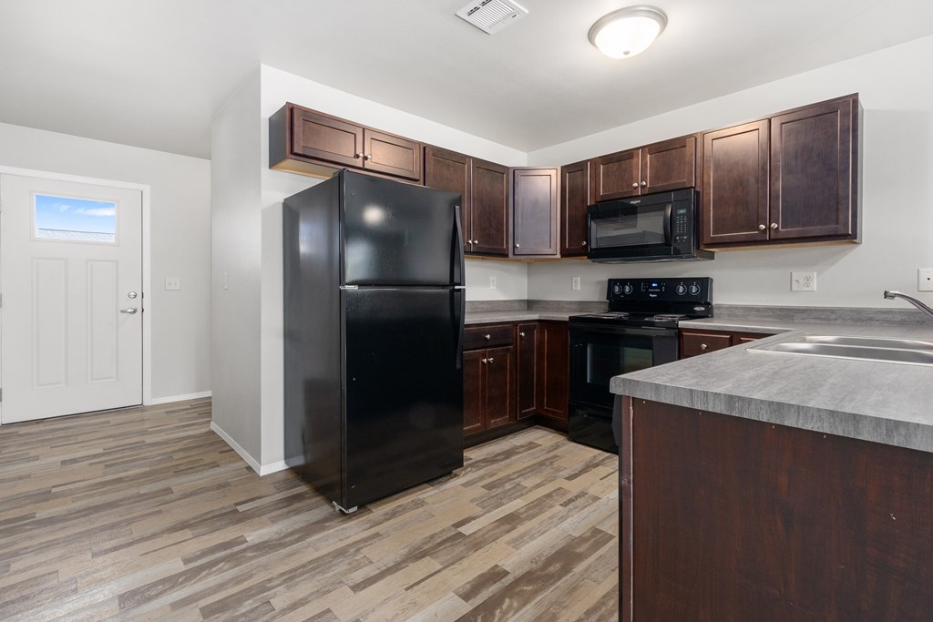 A black refrigerator stands in a kitchen with wooden cabinets and a marble countertop.