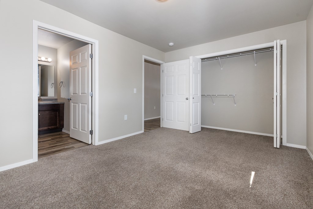 A carpeted room with a closet and a doorway leading to a kitchen.