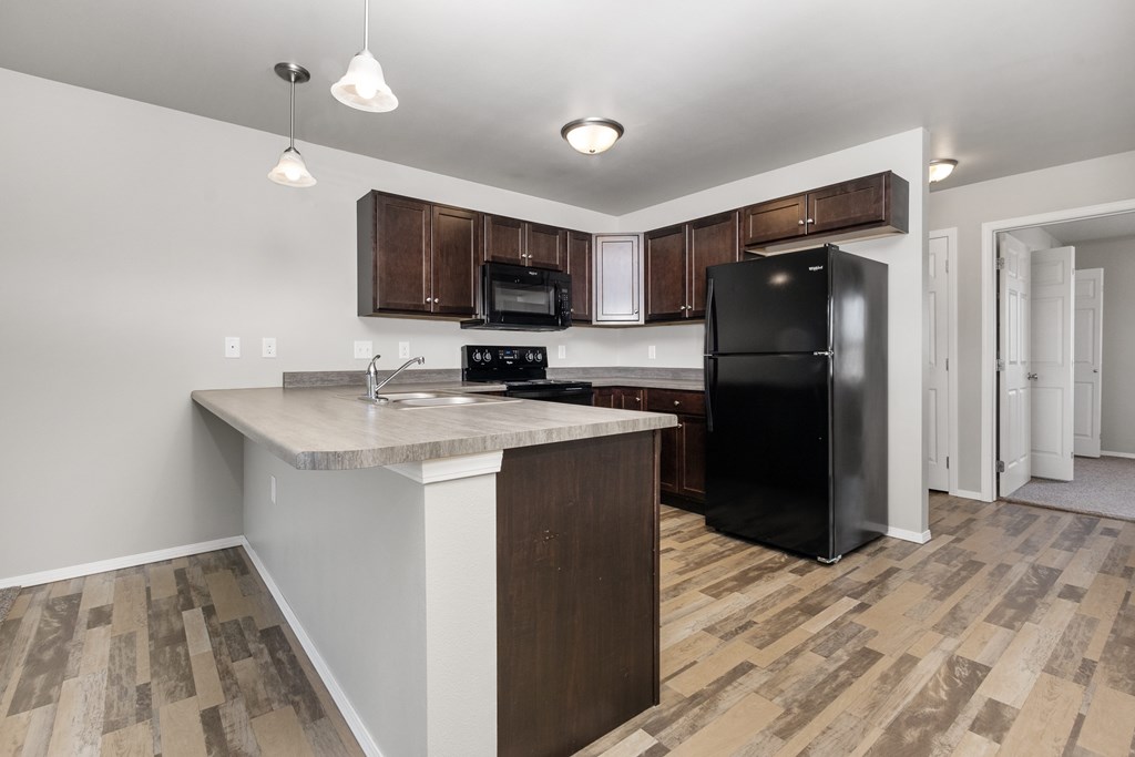 A kitchen with a black refrigerator and wooden cabinets.