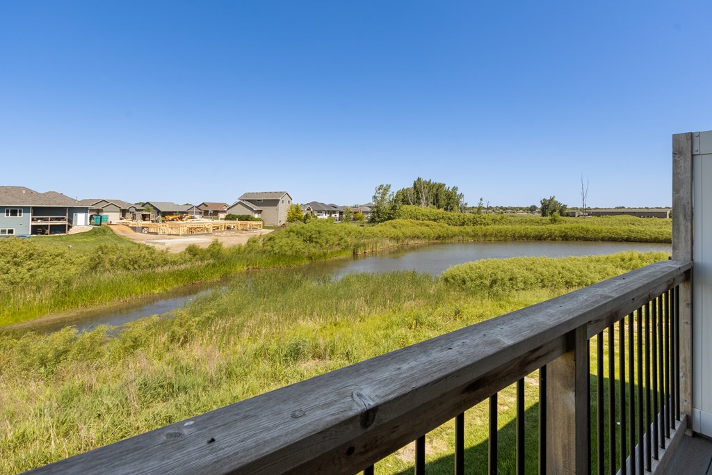 A wooden deck overlooks a grassy field with a river and houses in the distance.