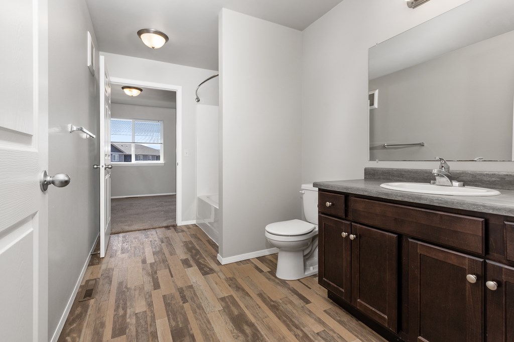 A bathroom with a toilet, sink, and wooden floors.