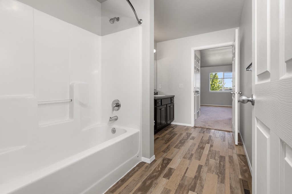 A white bathroom with a wooden floor and a white tub.