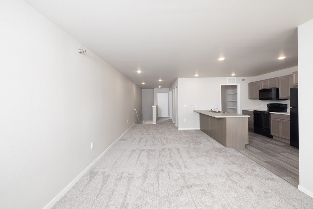 A spacious room with a carpeted floor and a kitchen area in the background.