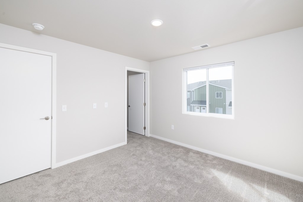 A white room with a carpeted floor and a window showing a house outside.