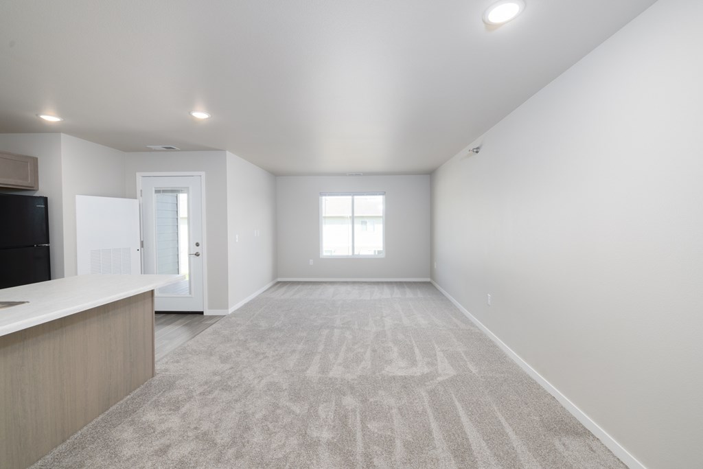A spacious, empty room with a carpeted floor and a window.