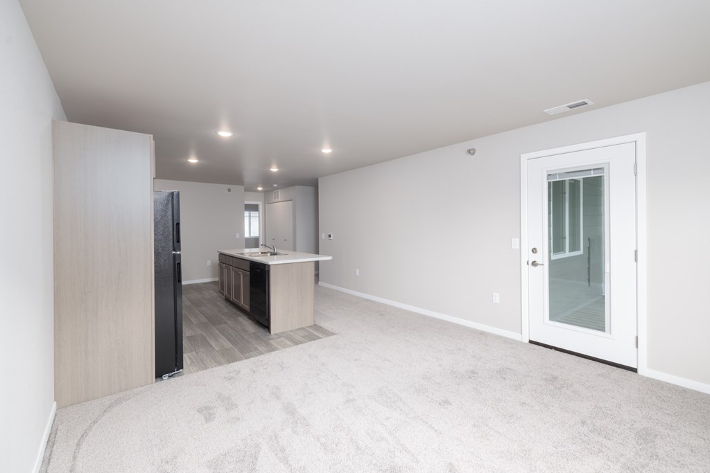 A spacious, empty room with a carpeted floor and a door leading to a bathroom.